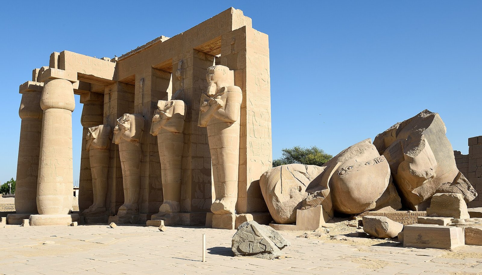 Coloso caido de Ramses II junto a los pilares osiriacos en pie del templo funerario del Ramesseum en Luxor bajo cielo despejado, Egipto