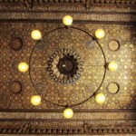 Techo ornamentado con lamparas doradas encendidas y detalles geometricos islamicos en un palacio historico de El Cairo, Egipto, que evoca el lujo del viaje
