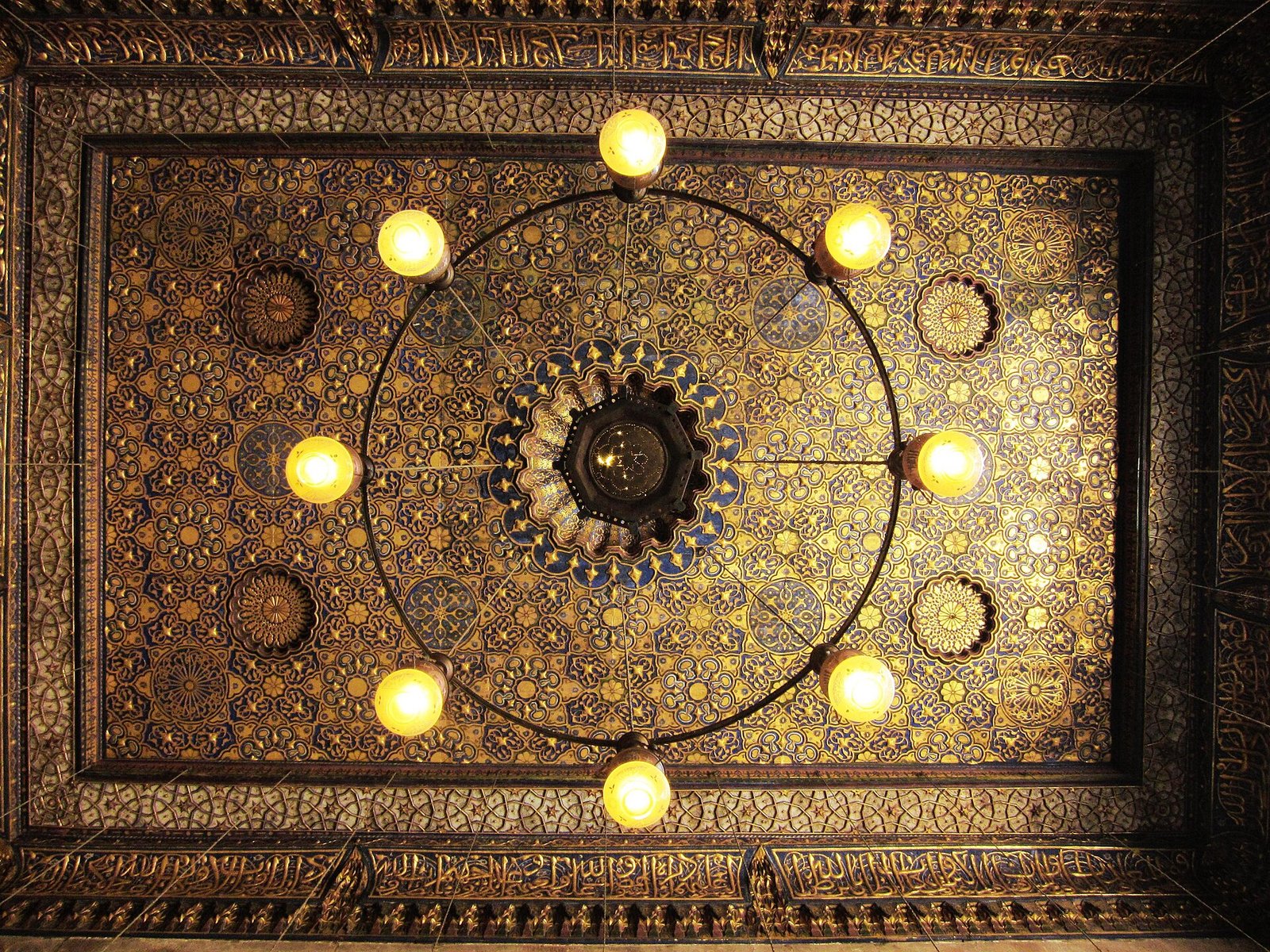 Techo ornamentado con lamparas doradas encendidas y detalles geometricos islamicos en un palacio historico de El Cairo, Egipto, que evoca el lujo del viaje