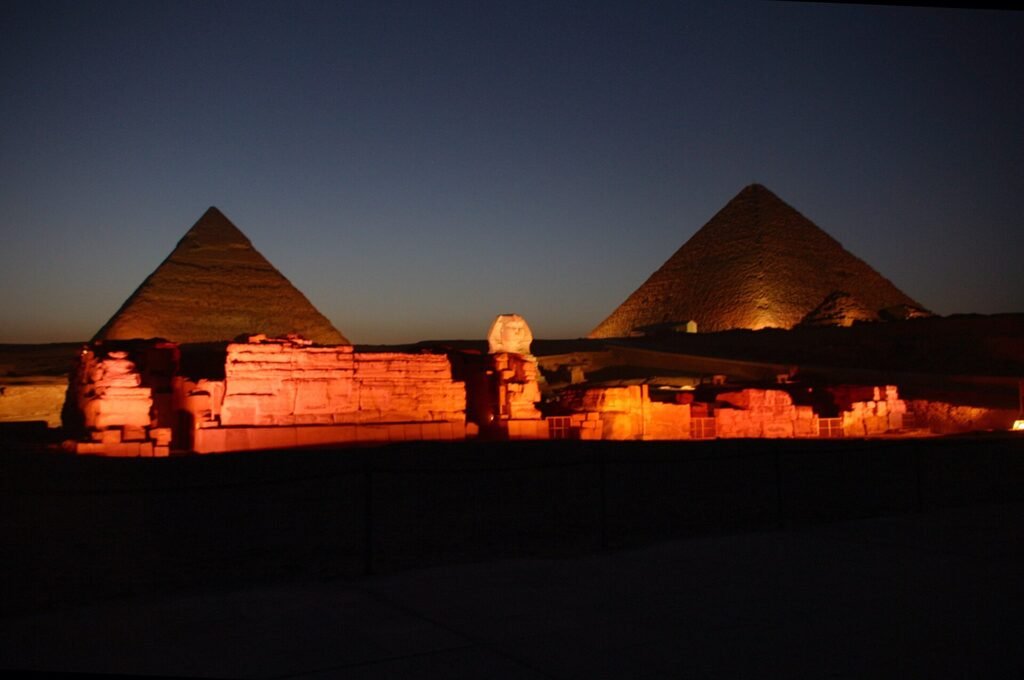 La Esfinge y dos piramides de Giza con iluminacion calida dorada durante el espectaculo nocturno de luz y sonido, recortadas contra un cielo azul profundo al anochecer