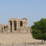 Templo de Kom Ombo a orillas del Nilo en Egipto, con sus columnas talladas enmarcadas por arboles verdes y cielo calido y despejado