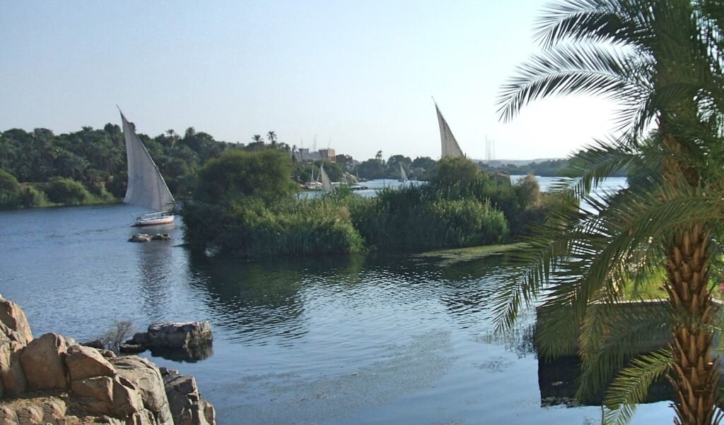 Faluca de vela blanca navegando por el Nilo entre palmeras e islas verdes en Asuan, Egipto
