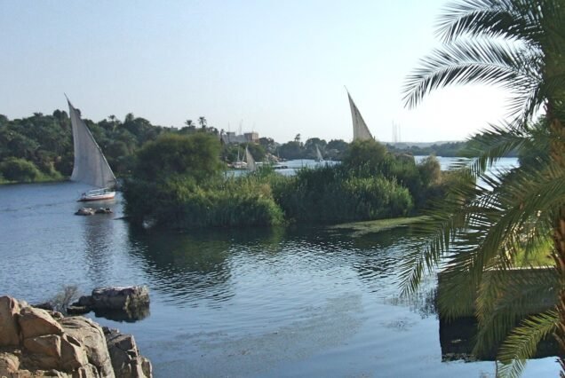 Faluca de vela blanca navegando por el Nilo entre palmeras e islas verdes en Asuan, Egipto