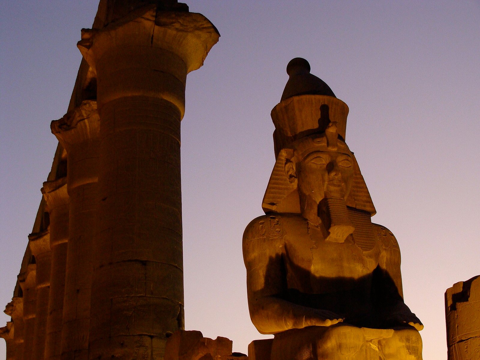 Coloso monumental de Ramses II en el templo de Luxor iluminado por la luz dorada del atardecer junto a una gran columna de papiro bajo cielo azul