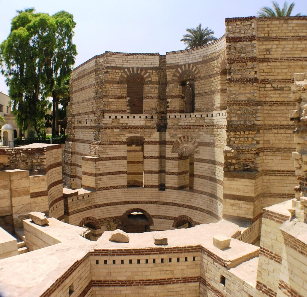 Las torres redondas de piedra romana de la Fortaleza de Babilonia en El Cairo Copto, Egipto, con bandas de ladrillo rojo, arcos ciegos y palmeras bajo cielo azul
