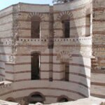 Vista frontal del muro curvo de la antigua fortaleza romana de Babilonia en El Cairo, Egipto, con caliza blanca, hileras de ladrillo rojo y ventanas arqueadas