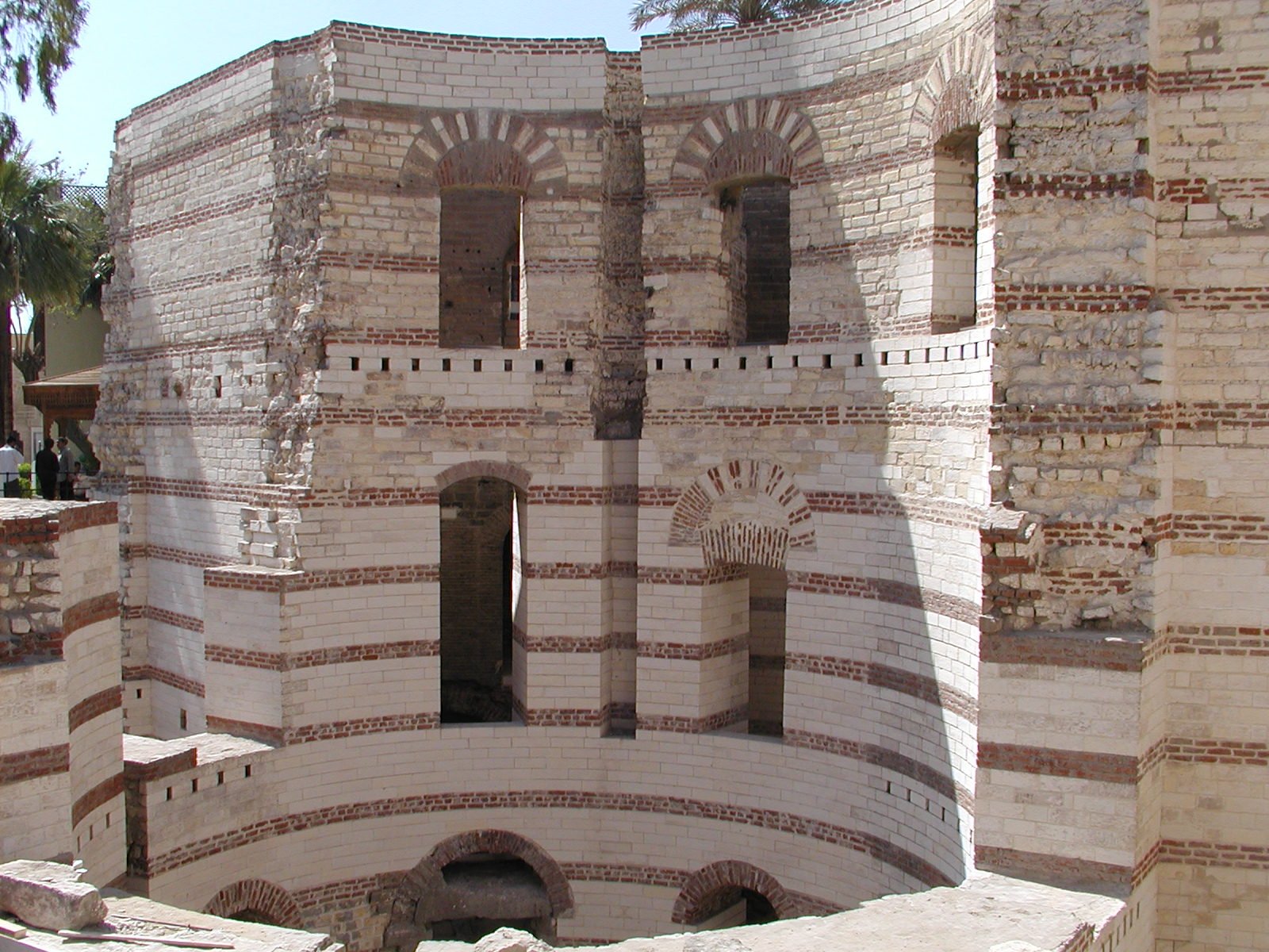 Vista frontal del muro curvo de la antigua fortaleza romana de Babilonia en El Cairo, Egipto, con caliza blanca, hileras de ladrillo rojo y ventanas arqueadas