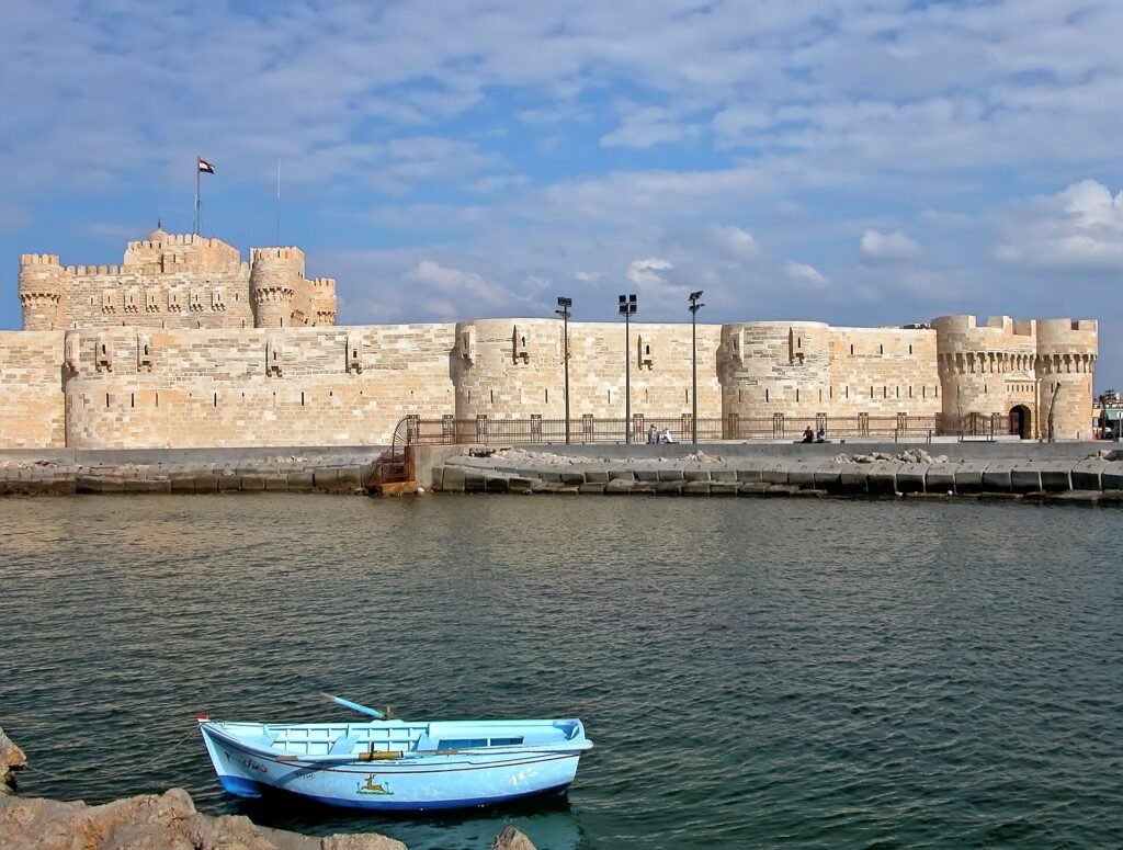 La fortaleza de Qaitbay en Alejandria, Egipto, vista desde el agua con un pequeno bote azul y el mar Mediterraneo en primer plano bajo cielo despejado