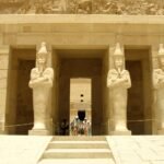 Colosos osiriacos de Hatshepsut con brazos cruzados flanqueando el portico de columnas del templo de Deir el-Bahari, con escalinata de piedra clara en primer plano