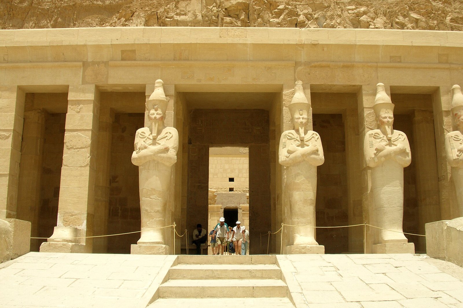 Colosos osiriacos de Hatshepsut con brazos cruzados flanqueando el portico de columnas del templo de Deir el-Bahari, con escalinata de piedra clara en primer plano
