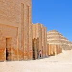 Columnata de entrada del complejo funerario de Zoser en Saqqara, con muros de piedra caliza dorada y columnas acanaladas disenadas por Imhotep, y la Pirámide Escalonada al fondo