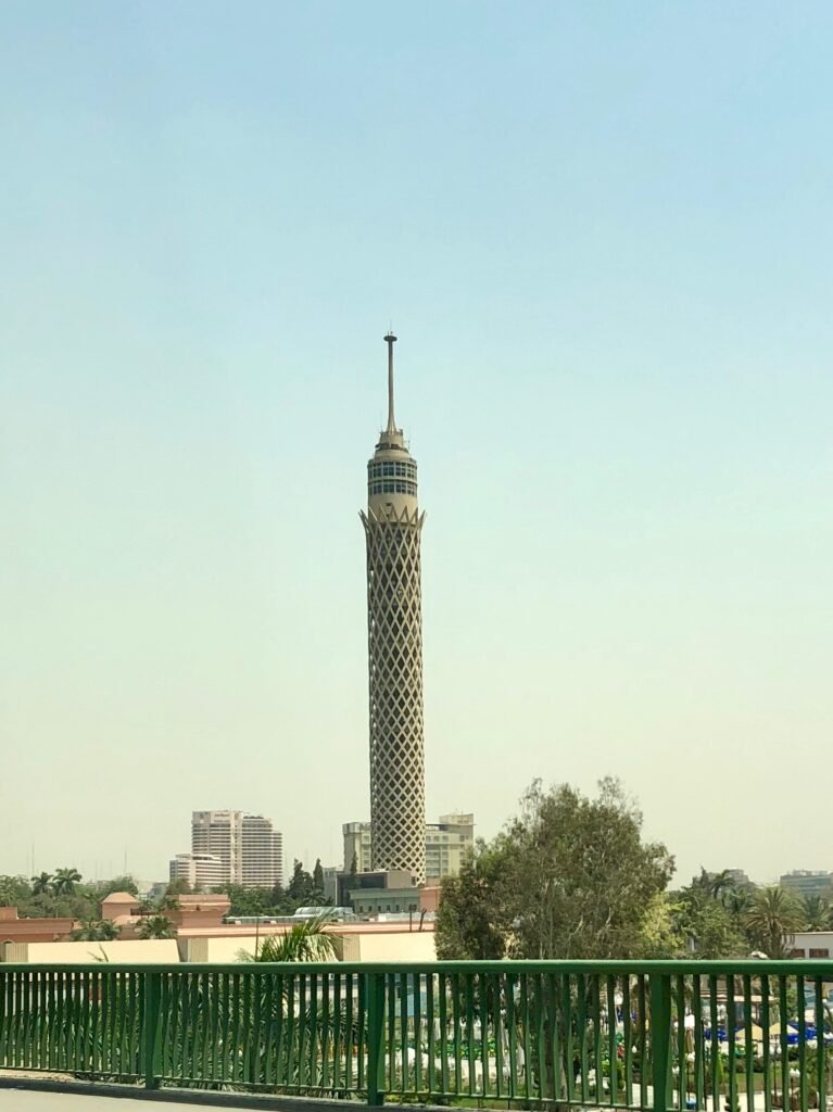 Torre de El Cairo iluminada por el sol sobre el horizonte de la ciudad con palmeras y cielo azul claro, vista urbana premium de Egipto