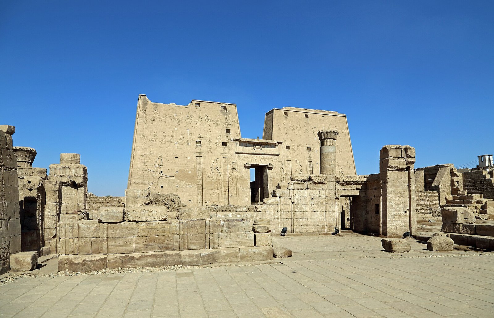 Gran pilono del templo de Edfu en Egipto con relieves tallados y patio de piedra bajo un cielo azul intenso patrimonio faraonico