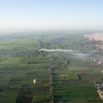 Vista aerea amplia del valle del Nilo en Egipto con un mosaico de campos verdes que limita con el desierto dorado y globos aerostaticos al amanecer