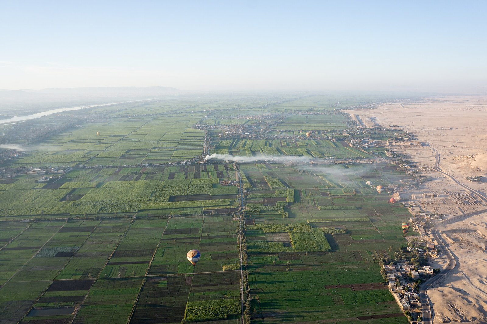 Vista aerea amplia del valle del Nilo en Egipto con un mosaico de campos verdes que limita con el desierto dorado y globos aerostaticos al amanecer