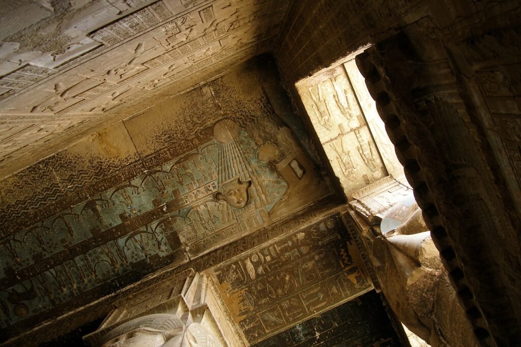 Muro y techo de templo egipcio cubierto de jeroglificos pintados con color conservado en azul, ocre y verde, iluminados por luz calida natural