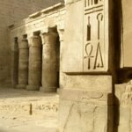 A temple courtyard corner at Medinet Habu with deeply cut hieroglyphs including a large ankh on the near pillar and a colonnade running away behind
