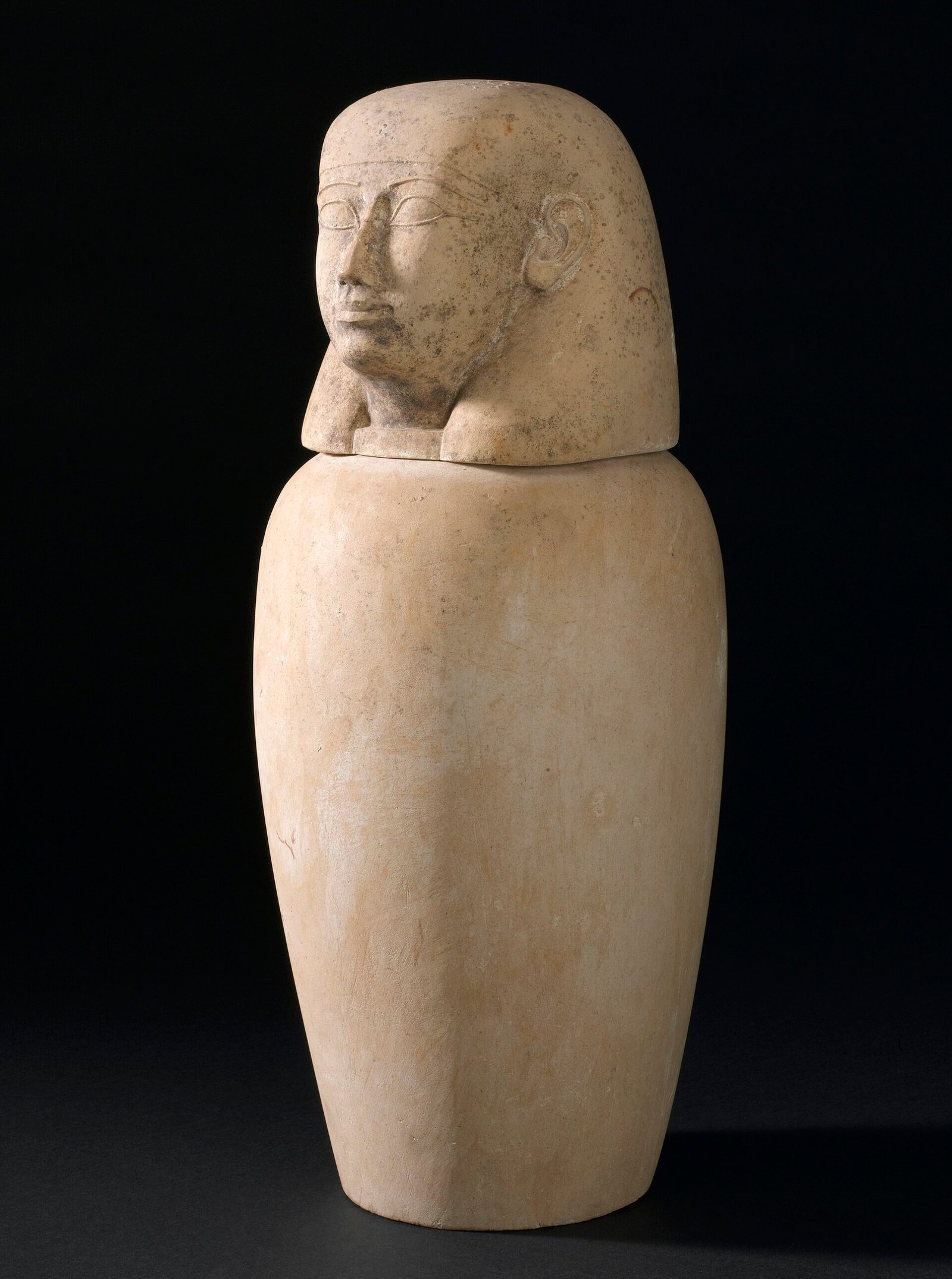 Vaso canopo egipcio de alabastro con tapa tallada en forma de cabeza humana sobre fondo oscuro, pieza funeraria del antiguo proceso de momificacion