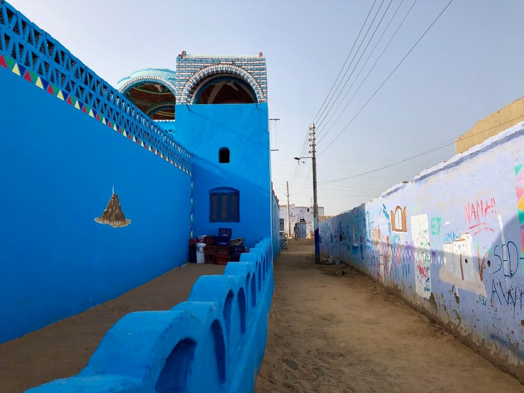 Callejon de un pueblo nubio en Egipto con casas pintadas de azul cobalto intenso, cupula y cenefa de triangulos de colores bajo cielo despejado, rincon muy fotogenico