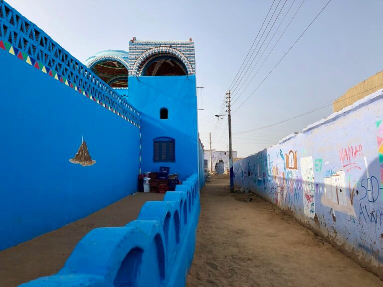 Callejon de un pueblo nubio en Egipto con casas pintadas de azul cobalto intenso, cupula y cenefa de triangulos de colores bajo cielo despejado, rincon muy fotogenico
