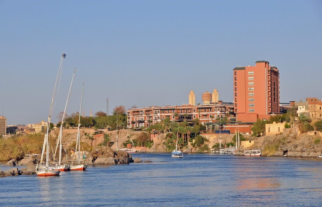 Feluccas con velas blancas en el Nilo de Asuan a la luz dorada del atardecer con hoteles sobre las rocas, escena romantica de luna de miel en Egipto