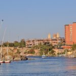 Feluccas con velas blancas en el Nilo de Asuan a la luz dorada del atardecer con hoteles sobre las rocas, escena romantica de luna de miel en Egipto