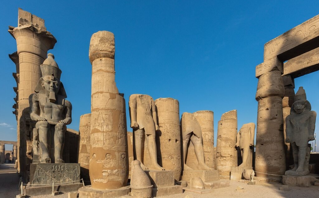 Columnas monumentales y estatuas colosales de Ramses en el patio del Templo de Luxor con jeroglificos bajo un cielo azul intenso en Egipto