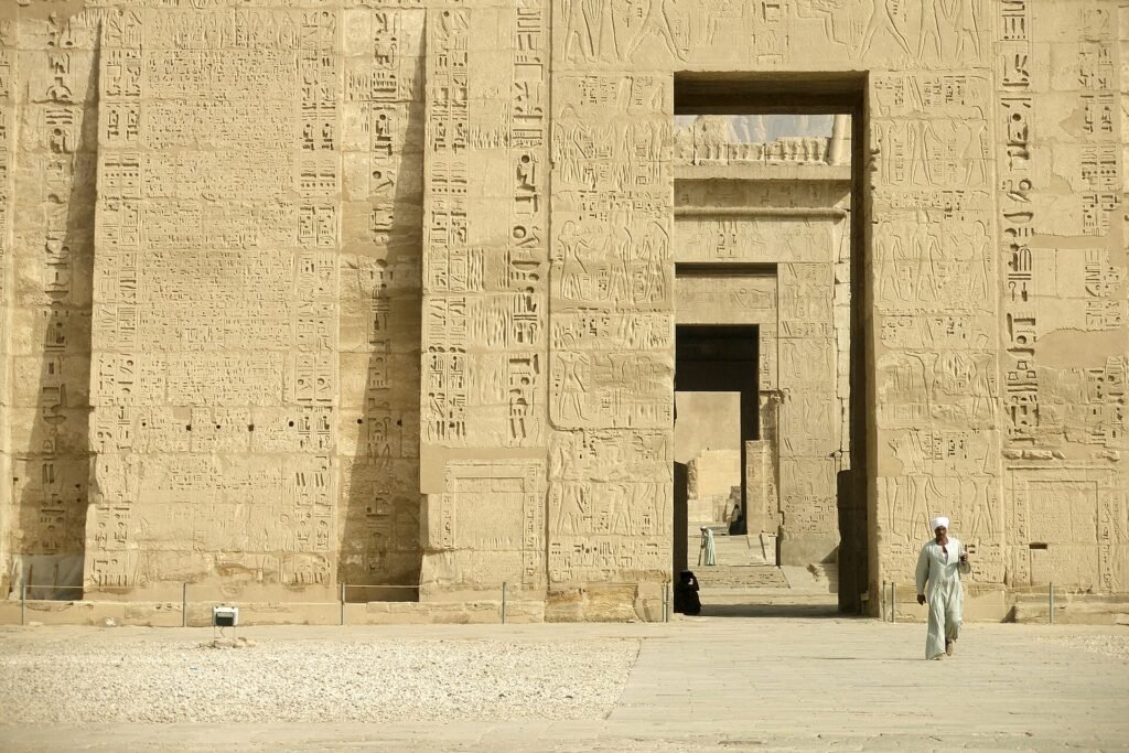 Gran pilono del templo de Medinet Habu en Luxor Egipto con relieves jeroglificos tallados en piedra dorada y portal central iluminado por luz calida