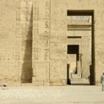 Gran pilono del templo de Medinet Habu en Luxor Egipto con relieves jeroglificos tallados en piedra dorada y portal central iluminado por luz calida