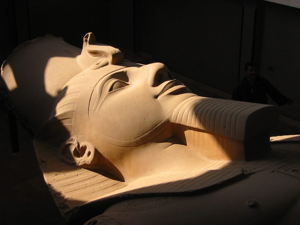 Cabeza colosal de la estatua yacente de Ramses II en piedra caliza iluminada con luz calida en el museo de Menfis, Egipto