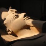 Cabeza colosal de la estatua yacente de Ramses II en piedra caliza iluminada con luz calida en el museo de Menfis, Egipto
