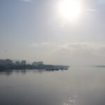 Amplia vista del rio Nilo en el Egipto medio al amanecer, con el sol brillando sobre el agua tranquila y la silueta de una ciudad ribereña a lo lejos