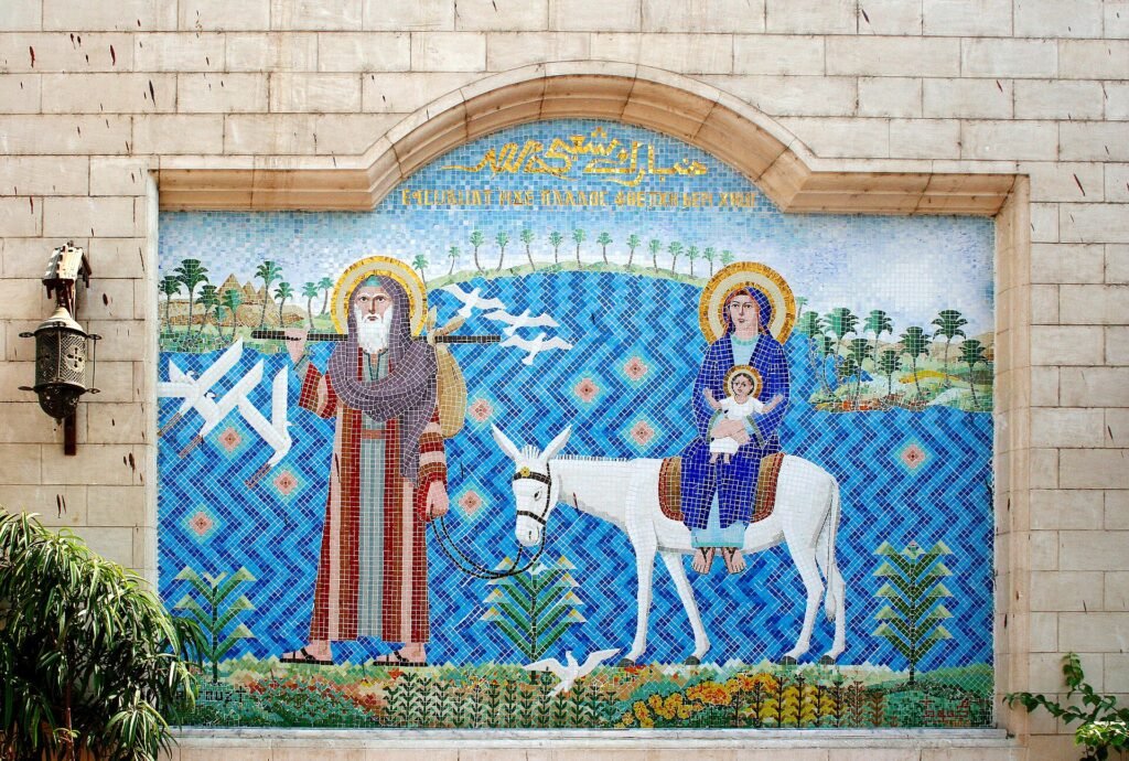 A large mosaic on a Coptic church wall in Cairo showing the Holy Family's flight into Egypt, Joseph leading a white donkey carrying Mary and the child, on a bright blue tiled ground