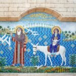 A large mosaic on a Coptic church wall in Cairo showing the Holy Family's flight into Egypt, Joseph leading a white donkey carrying Mary and the child, on a bright blue tiled ground