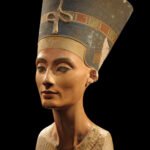 Busto policromado de la reina Nefertiti en vista de tres cuartos sobre fondo negro, con su alta corona azul y collar ancho de colores