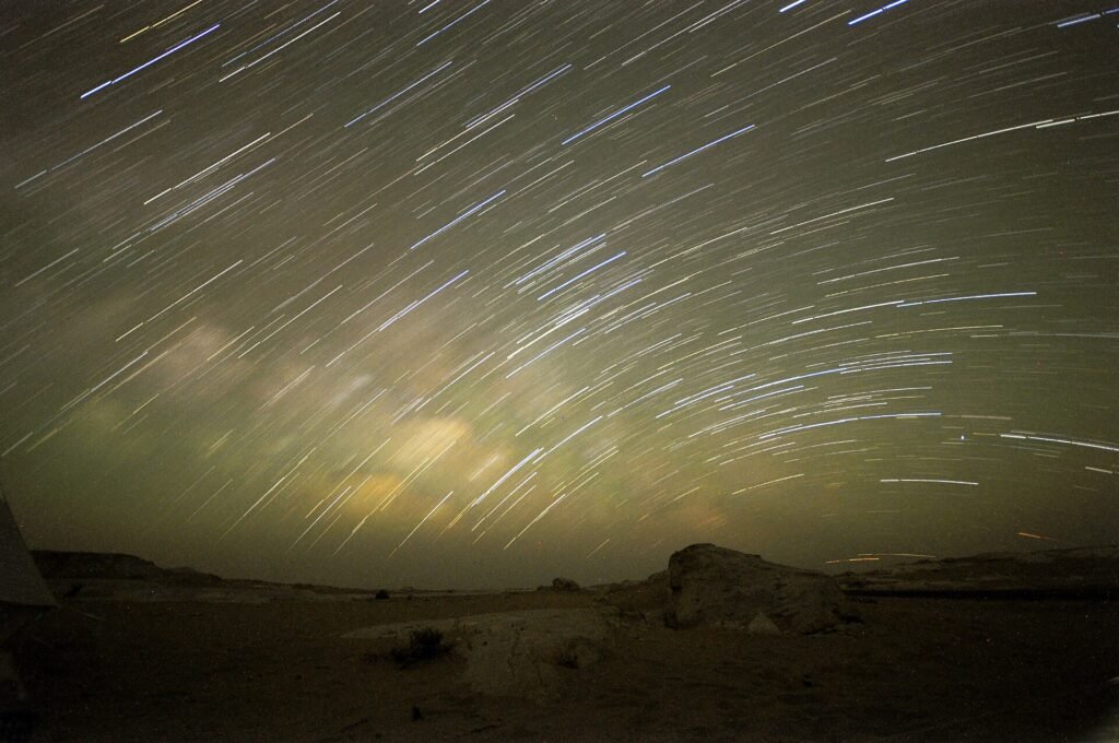 Cielo estrellado con largas estelas de estrellas sobre las formaciones de roca clara y las dunas del Desierto Blanco de Egipto durante una noche evocadora
