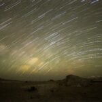 Cielo estrellado con largas estelas de estrellas sobre las formaciones de roca clara y las dunas del Desierto Blanco de Egipto durante una noche evocadora