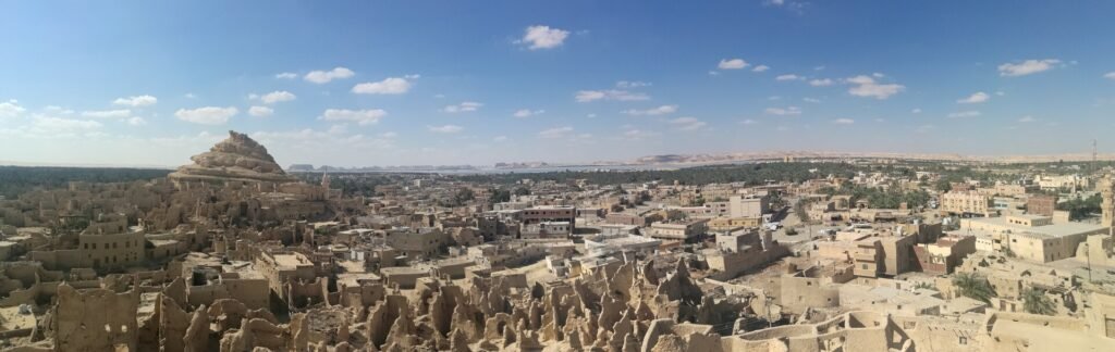 Vista panoramica del Oasis de Siwa en Egipto con la fortaleza de adobe de Shali, el palmeral verde y los lagos salados al fondo bajo cielo azul