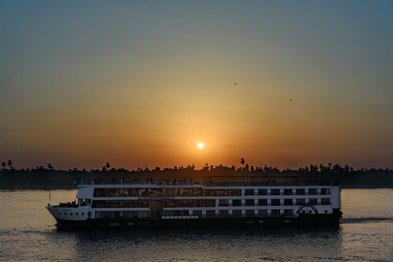 Crucero por el Nilo navegando al atardecer con el sol en el horizonte sobre palmeras, reflejo dorado en el agua durante un viaje por Egipto