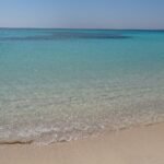 Orillas de aguas turquesa transparentes del Mar Rojo en Orange Bay con arena dorada fina y banadistas al fondo, ambiente de playa paradisiaca en Hurghada