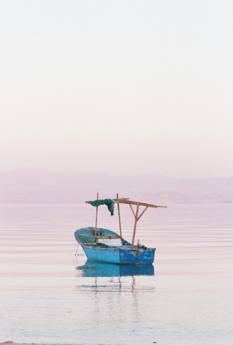 Barco de pesca tradicional de madera azul anclado en las aguas tranquilas del Mar Rojo al amanecer, con su estructura de sombra y montanas suaves al fondo