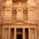 La fachada del Tesoro Al-Khazneh de Petra tallada en roca rosada en Jordania, con columnas y frontones iluminados por luz dorada calida
