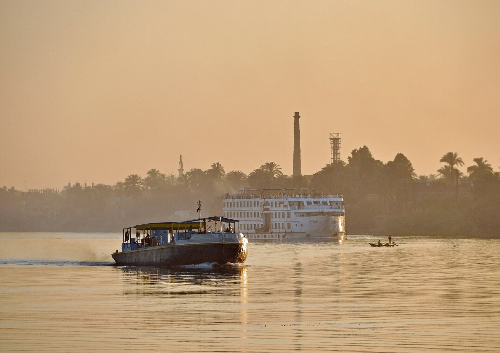 Crucero por el Nilo al atardecer dorado frente a la ribera de palmeras de Luxor en Egipto para planear el presupuesto de un viaje