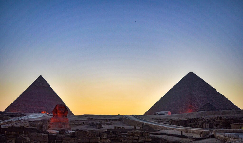 Las dos grandes piramides de Giza y la Gran Esfinge recortadas contra un cielo dorado al atardecer en Egipto, la imagen clasica del primer viaje