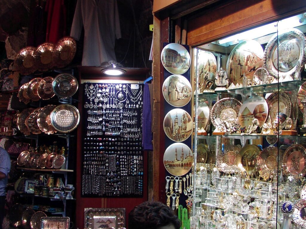 Tienda de souvenirs egipcios en un bazar con platos de cobre, bandejas de laton grabadas y collares colgantes, colores calidos y ambiente evocador