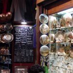 Tienda de souvenirs egipcios en un bazar con platos de cobre, bandejas de laton grabadas y collares colgantes, colores calidos y ambiente evocador