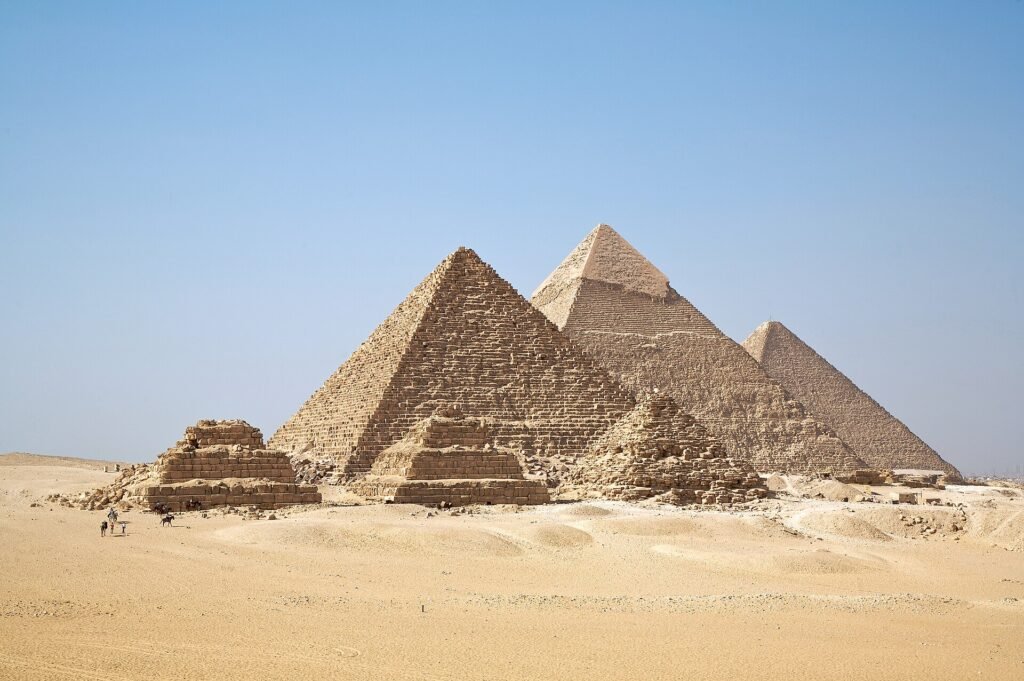 Las tres grandes piramides de Giza bajo un cielo azul despejado con arena dorada en primer plano cerca de El Cairo en Egipto