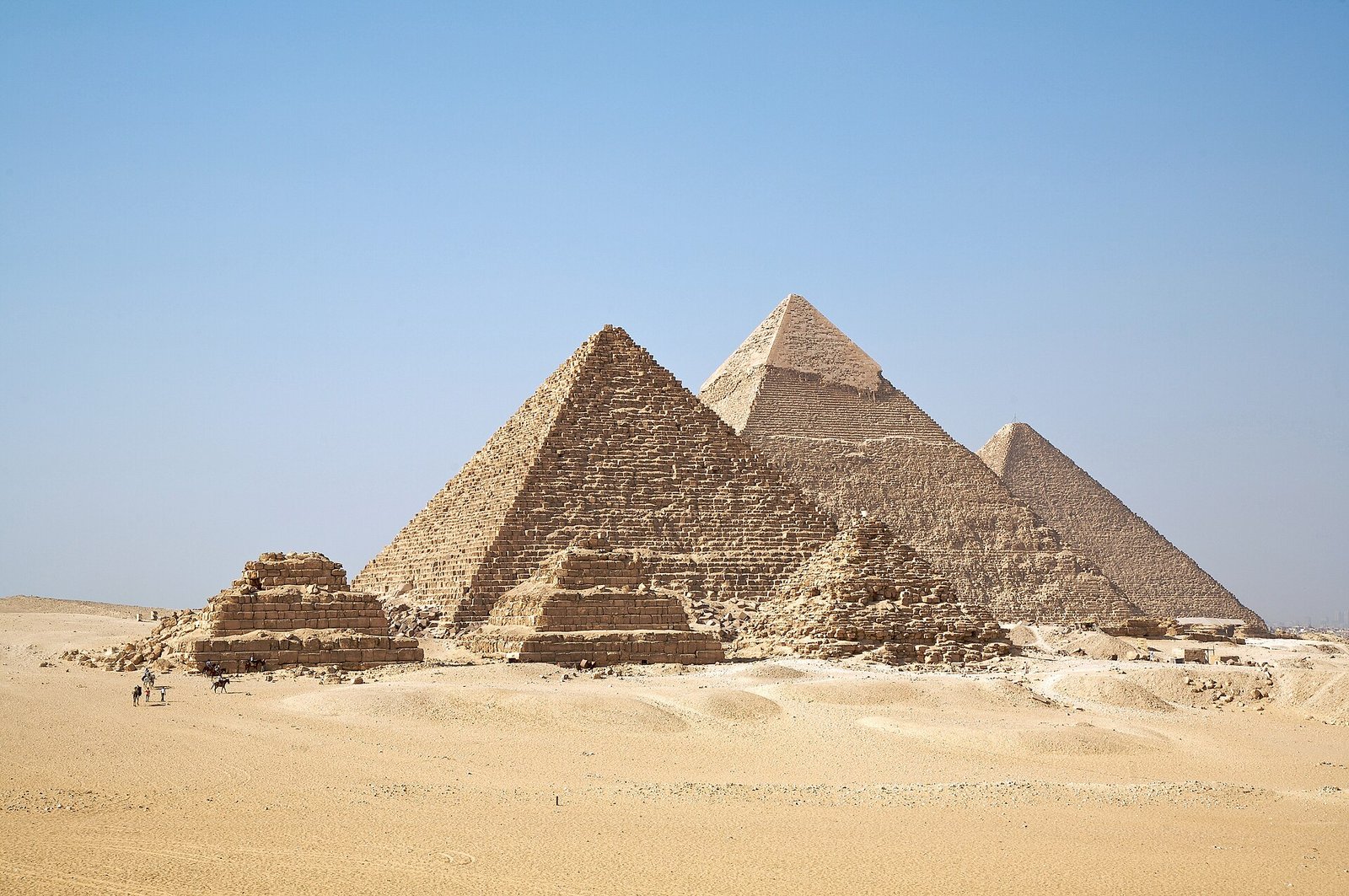Las tres grandes piramides de Giza bajo un cielo azul despejado con arena dorada en primer plano cerca de El Cairo en Egipto