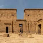 Fachada del primer pilono del templo de File en Asuan con relieves tallados y puerta central iluminados por luz dorada en Egipto