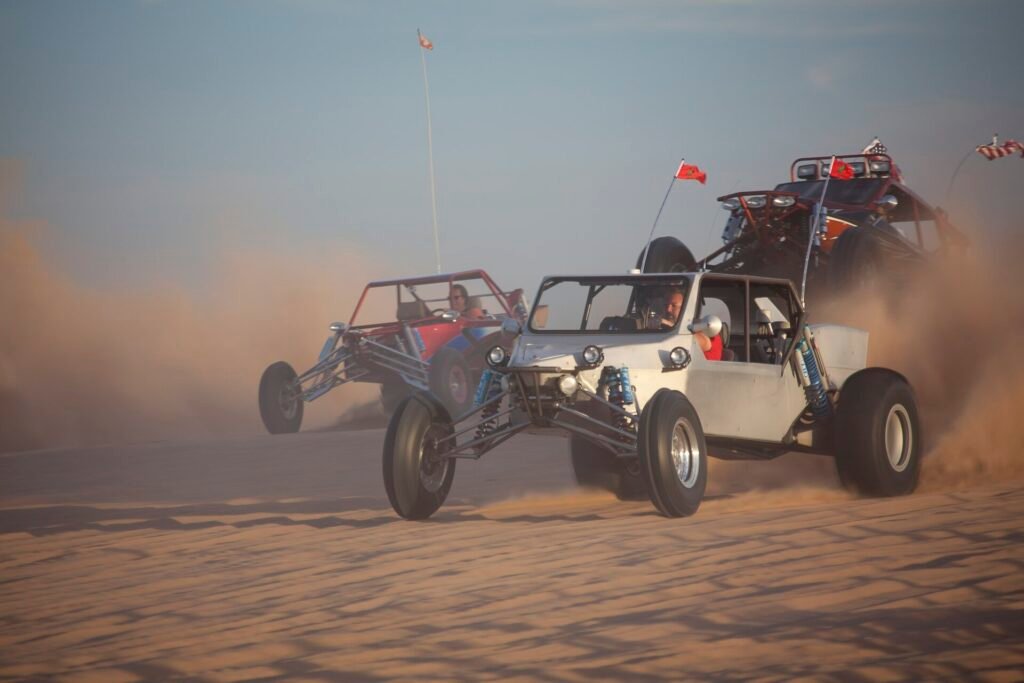 Dos buggies todoterreno cruzando a toda velocidad las dunas de arena del desierto levantando polvo, escena energica con luz dorada y colores premium